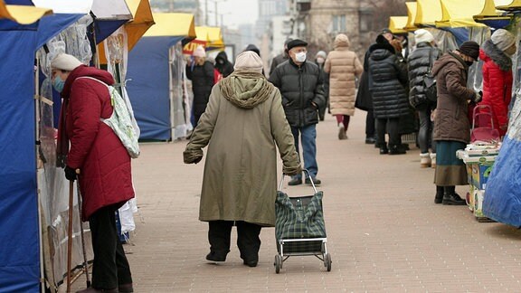 Eine Seniorin zieht einen Einkaufswagen über einen Markt.