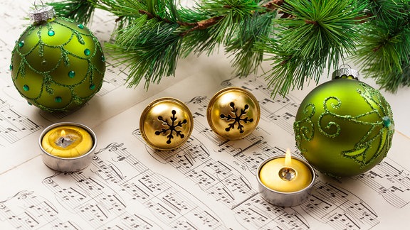 Weihnachtskugeln, ein Tannenzweig und Teelichter liegen auf einem Notenblatt. 