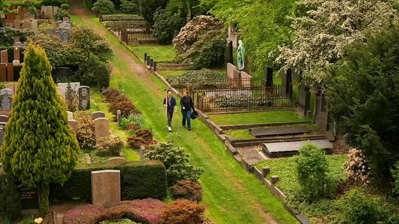 Zwei Menschen laufen mit Gartengeräten über den Annenfriedhof in Dresden.