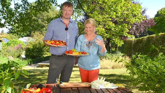Ein Mann und eine Frau halten Teller auf denen verschiedene Chilischoten liegen. 