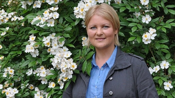 MDR Garten-Moderatorin Diana Fritzsche-Grimmig steht vor einem grünen Strauch mit weißen Blüten. 
