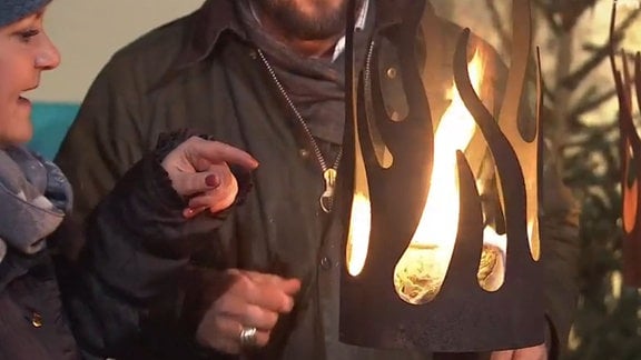 Ein zylinderförmige Fackel aus Cortenstahl in Form von stilisierten aufsteigenden Flammen, in der ein Feuer brennt