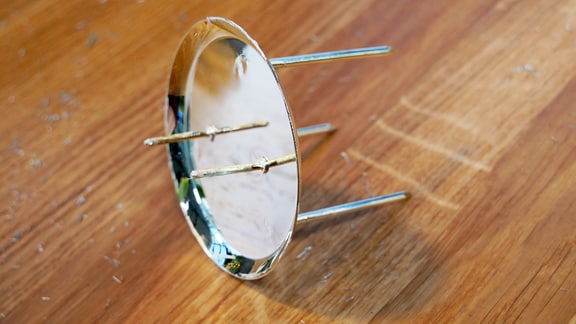 Ein dreibeiniger Kerzenteller für Stumpenkerzen. Aus dem Teller ragen zwei Nadeln hervor.