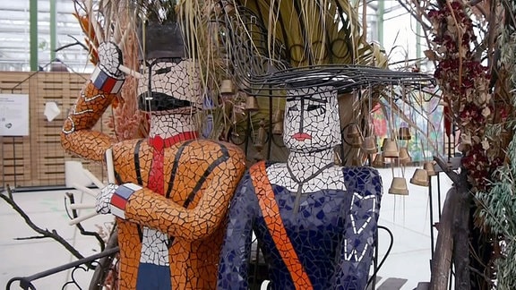 Zwei Keramikfiguren, Frau und Mann, in Grünpflanzendekoration.