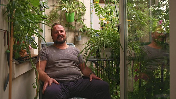 Ein Mann sitzt auf einem Balkon umgeben von Pflanzen