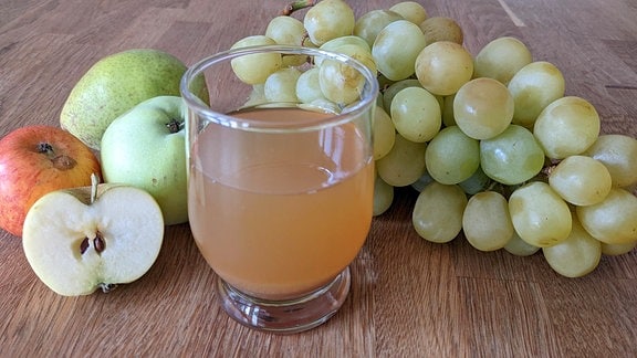 Ein Glas Apfelsaft auf dem Tisch mit Äpfeln und Weintrauben.