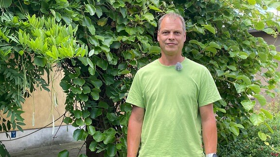 Matthias Pabst, langjähriger Mitarbeiter im Botanischen Garten Halle steht vor einem bewachsenen Laubengang.
