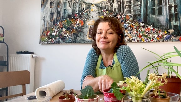 Gärtnerin Brigitte Goss sitzt an einem Tisch auf dem ausgetriebene Gemüsereste liegen. 
