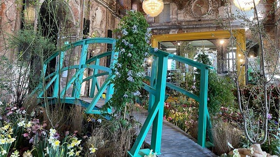 Eine blaue Holzbrücke mit Blumenarrangements in der Ausstellung "Dresdner Frühling im Palais"