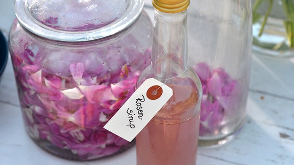 Eine Flasche mit einer Rosa Flüssigkeit und einem kleinen Schild auf dem Rosensirup steht. 