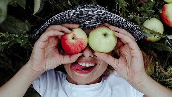Ein Kind hält Äpfel vor seine Augen