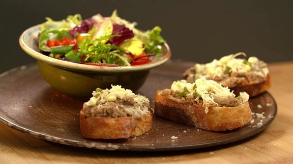 Eine Schüssel mit gemischtem Salat und drei Scheiben Weißbrot mit Aufstrich aus Bohnencreme