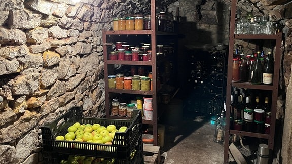 Ein Kellerraum mit Obststiegen auf dem Boden und eingewecktem Obst und Gemüse in Regalen.