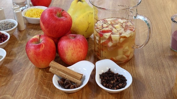 Auf einem Tisch liegen Äpfel, Gewürze und Öl