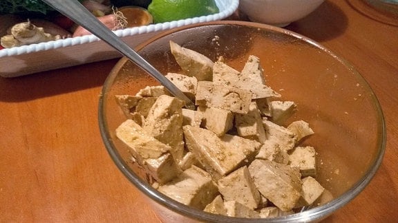 Tofu mariniert in einer Glasschüssel mit Rührlöffel.
