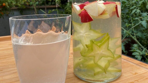 Eine Karaffe mit Wasser. Darin schwimmen Früchte. Das Wasser wird in ein Glas eingeschänkt.