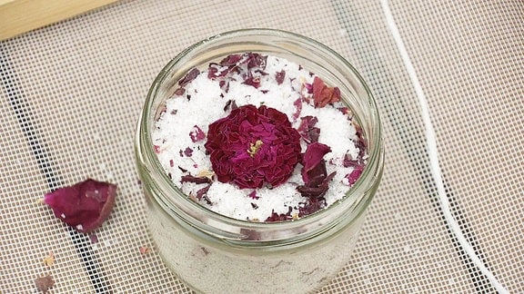 Getrocknete Rosenblüten liegen auf Salz in einem geöffneten Schraubglas