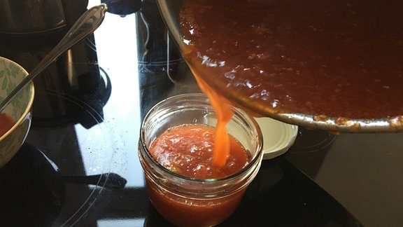 Heiße Tomatenmarmelade aus Topf in Schraubdeckel-Glas umfüllen