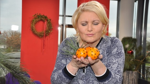 Eine Frau hält Orangen mit Nelken und einen Tannenzwei in der Hand. Sie riecht daran.  
