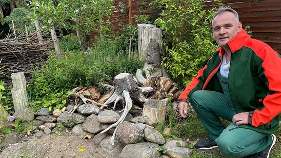 Ein Mann kniet neben einem Hügel aus Holz und Steinen. Das ist eine Eidechsenburg.