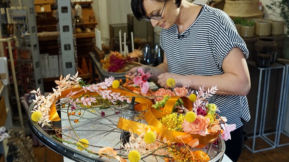 Floristin Juliane Müller arbeitet an Deko mit Fahrrad-Felge, Blumen und Orangen