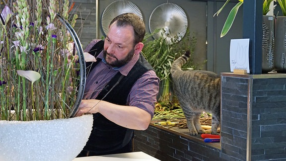 Florist Thorsten Wösthaus arbeitet an Blumen-Gesteck mit Fahrrad-Felge