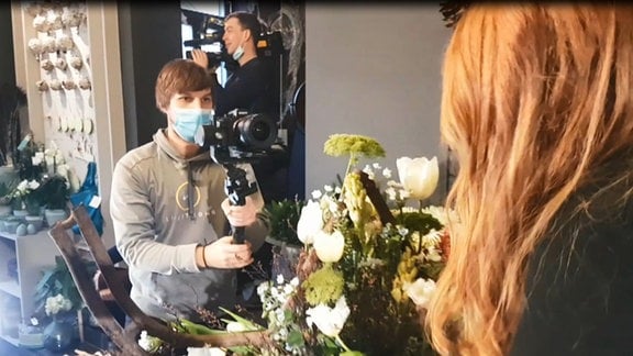 Ein junger Mann filmt eine Floristin beim Arbeiten. Im Hintergrund steht ein zweiter Mann mit einer Kamera.