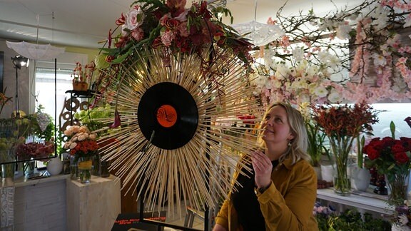 Eine Frau steckt Blüten in einen Strahlenkranz aus Holzstäbchen
