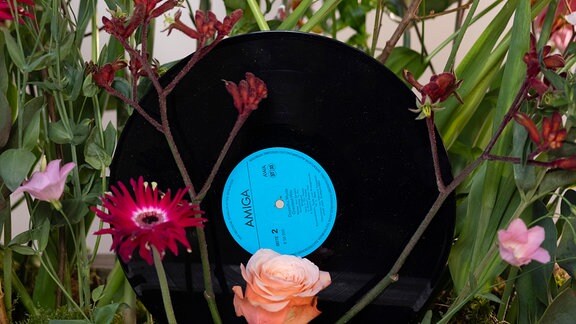 Eine Schallplatte steckt in einem Arrangement bunter Blumen.
