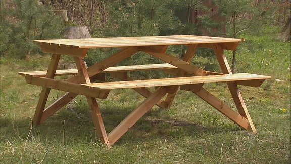 Ein Picknicktisch mit integrierten Sitzbänken steht auf einer Wiese.