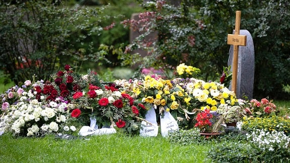Ein mit vielen Blumen geschmücktes Grab auf einem Friedhof.
