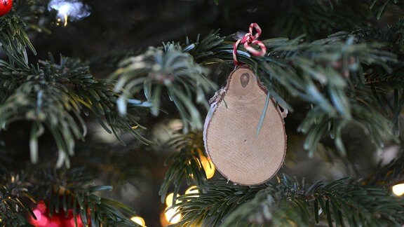 An einem Weihnachtsbaum hängt eine Holzscheibe 