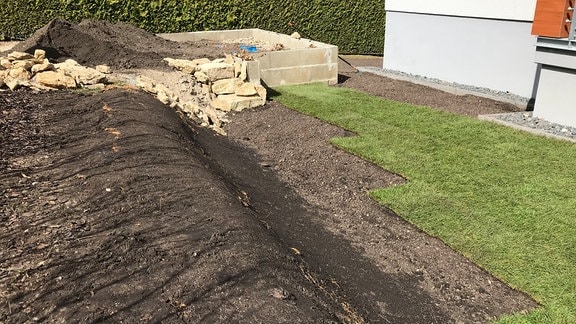 Ein Garten mit einer teils mit Fertigrasen belegten Fläche und einem Wall aus Erde 