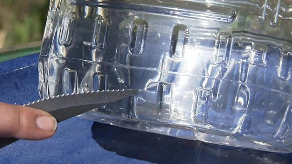 Mit der Spitze eines scharfen Messers wird ein Schlitz in den unteren Bereich einer Plastikflasche gebohrt