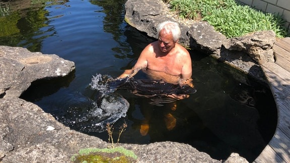 Hobbygärtner Wolfgang Kohlhepp steht in seinem Fischteich und hält einen Stör in den Händen. 