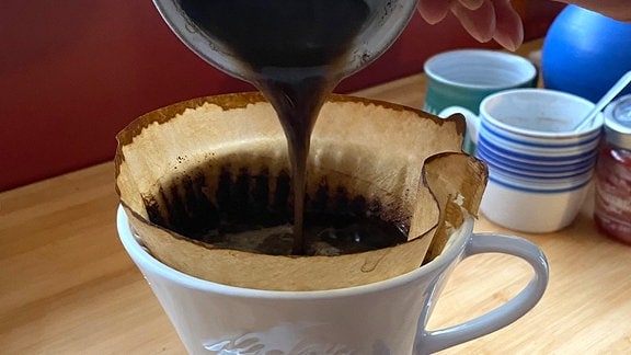 Aus einer Kaffeetasse wird der Satz in einen Filter gegossen  