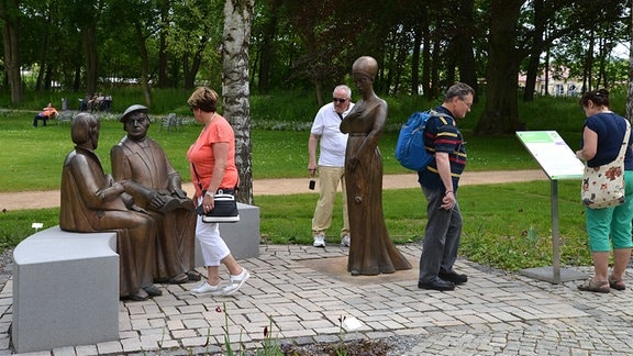 Menschen spazieren auf einer Promenade in einem Park. 