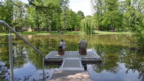 Zwei Menschen sitzen auf einem schwimmenden Steg auf einem Teich.