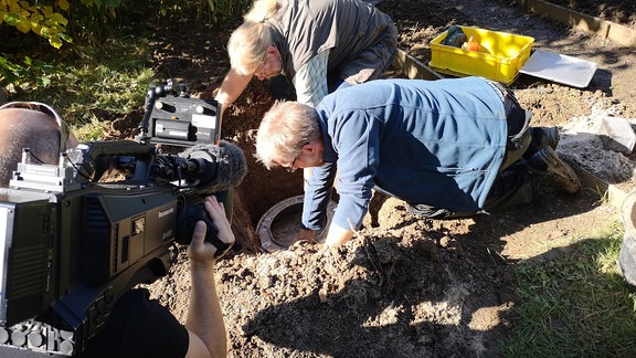 Zwei Männer hiefen eine Wäschetrommel in ein Loch im Boden.   
