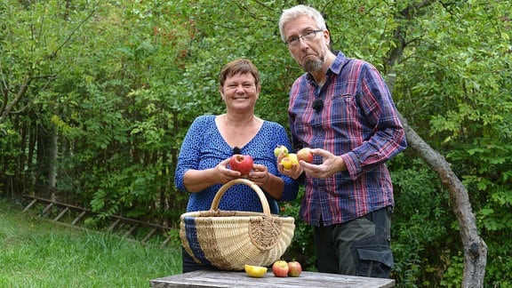 Hobbygärtner Jörg Heiß und Obstbaumexpertin Monika Möhler stehen an einem Tisch und halten Äpfel in den Händen