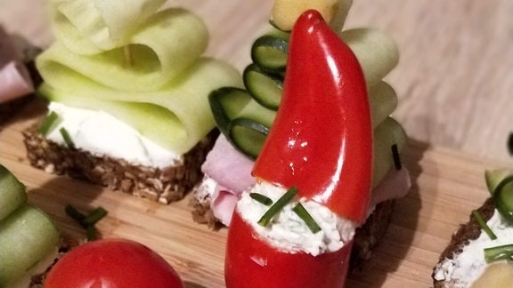Aufgeschnittene Cocktailtomate mit einer Mozarellakugel gefüllt. Auf dem weißen Kopf steckt eine Minipaprika. Das gemüse sieht aus wie ein Weihnachtsmann.  
