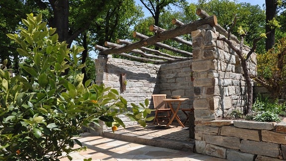 Aus Naturstein gemauerte Pergola mit einer Decke aus ungeschältem Rundholz.  