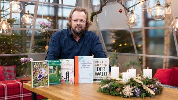 Ein Mann steht hinter einem Tisch. Darauf sind fünf Bücher neben einem Adventskranz präsentiert.