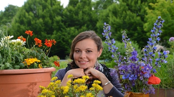 Junge Frau schaut zwischen Blumentöpfen mit bunten Blumen hindurch
