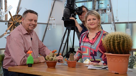 Kakteenexperte Ulrich Haage und Diana Fritzsche-Grimmig stehen im Fernsehstudio. Über ihre Schultern filmt ein Kameramann.  