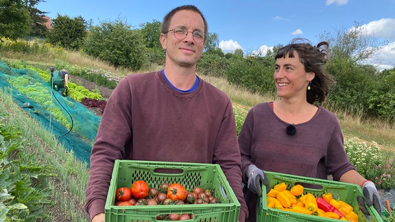 Ein Mann und eine Frau auf einem Feld halten Gemüsekisten im Arm.