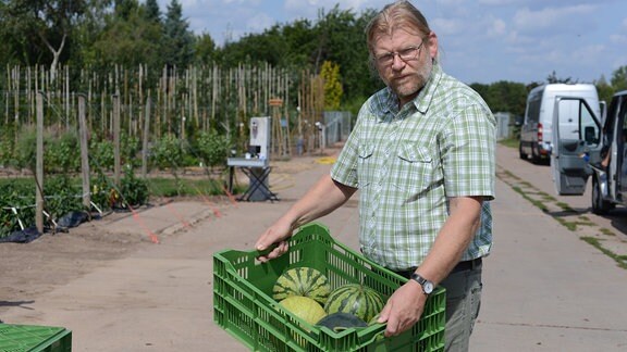 Gemüseexperte Martin Krumbein trägt eine Kiste mit Wassermelonen 