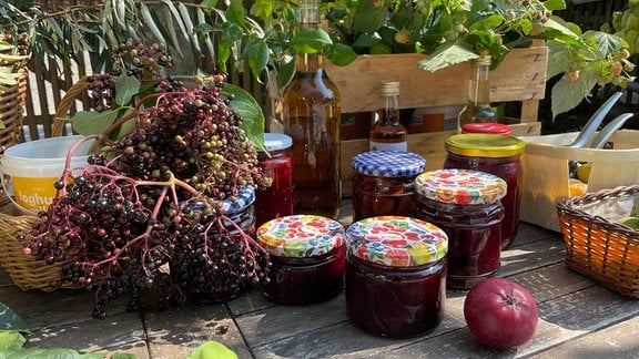 Holunderbeeren, Gläser mit Holundergelee und andere Wildfrüchte liegen auf einem Tisch.