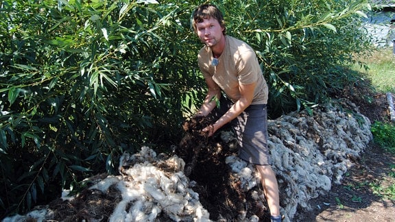 Permakultur-Gärtner Hendrik Noßmann legt Schafwolle auf Komposthaufen