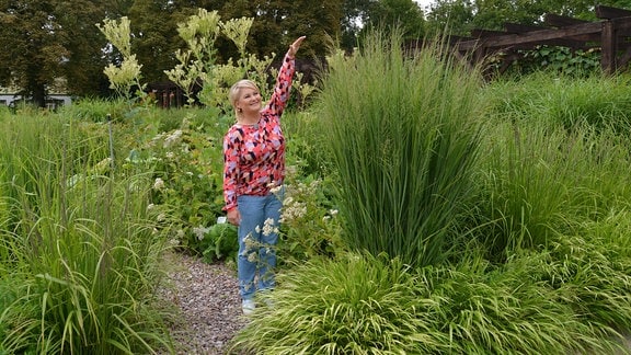 Moderatorin Diana Fritzsche Grimmig steht neben einem Gras, das sie überragt. 